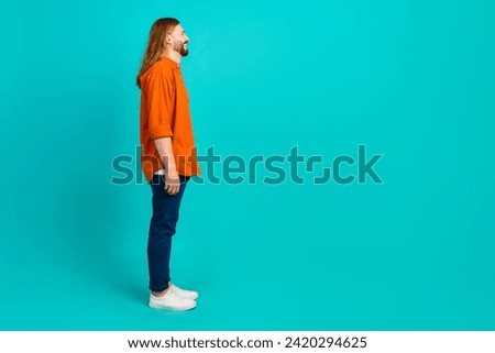 Side photo of optimistic blond hair guy in orange shirt looking at billboard advertisement place isolated on cyan color background