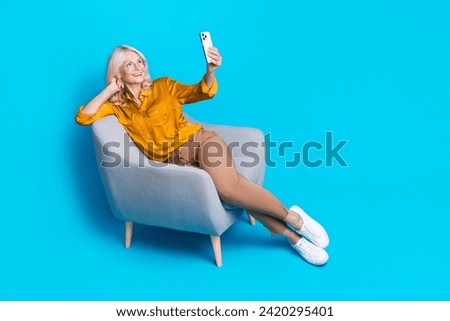 Full size photo of pretty retired female sit armchair video call dressed stylish yellow satin outfit isolated on blue color background