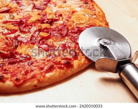 Metal pizza cutter by cooked cheese and tomato sauce thin Italian pizza on a wooden cutting board. Fast food meal for cooking in oven with basic products