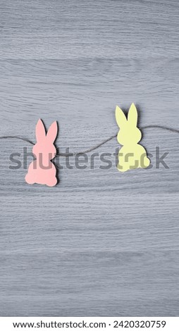 Garland with rabbits. Two silhouettes of bunnies cut out of colored paper on a gray wooden background. Vertical photo.