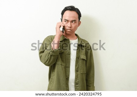 portrait of an Asian man in green jacket holding or communicating using a smartphone. gesture of Indonesian man communicating using smartphone on isolated white background