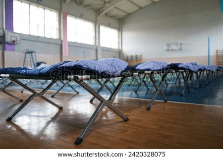 Cots with sleeping bags are placed in the school gym during an emergency Royalty-Free Stock Photo #2420328075