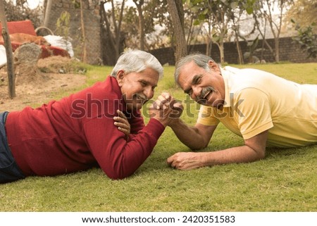 Indian senior friends playing arm wrestle together at park.