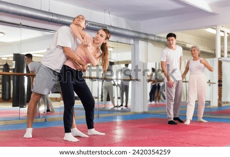 Focused young girl practicing basic protection skills with male opponent during self defense course in gym, trying to escape rear bear hug technique, striking with elbow to chin.. Royalty-Free Stock Photo #2420354259