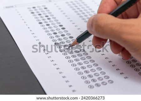 Hand filling out an exam answer sheet with a pencil, concept for public and entrance exams. Royalty-Free Stock Photo #2420366273
