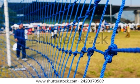 Close-up view of a rope net used as a goal net on a soccer field. Background of a football field in the middle of an open air amusement park.