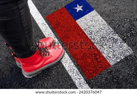 a woman with a boots standing on asphalt next to flag of Chile and border 