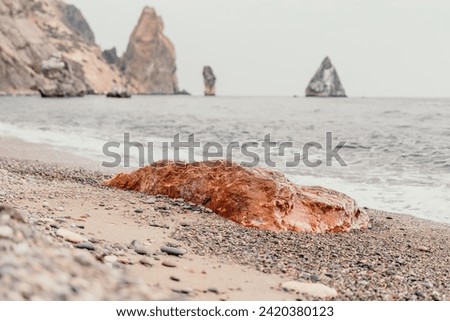 Large red jasper rock on the beach, with the sea in the background. Big Red Jasper Stone Close Up Royalty-Free Stock Photo #2420380123