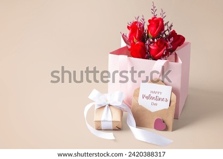 Happy valentine day card and envelope with gift box and rose in paper bag on beige background, copy space
