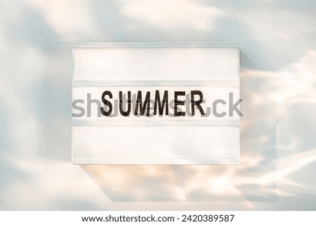A minimalistic lightbox displays bold black letters spelling out SUMMER, capturing the essence of the season with a dreamy sky backdrop.