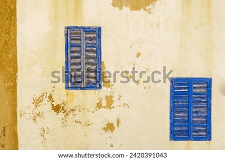 View of blue windows and shutters on an old house wall with pilling white paint. Essaouira (Mogador), Morocco Royalty-Free Stock Photo #2420391043