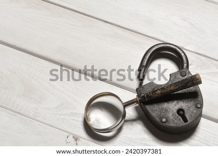 Old padlock and magnifying glass on the wooden desk table background. Secret information concept. Looking for the answers. Searching of clues concept. Royalty-Free Stock Photo #2420397381