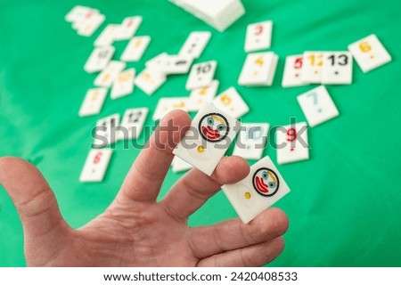Male hand holding two joker plastic tiles from the game rummikub, rummicub or  okey in Turkey o green background