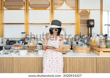 Hotel magazine cover photo There was an Asian female tourist who was a guest relaxing in front of the food section. Using a laptop to work, wearing a dress, hat, glasses, and relaxing on vacation.