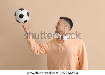 Happy young man with soccer ball on beige background