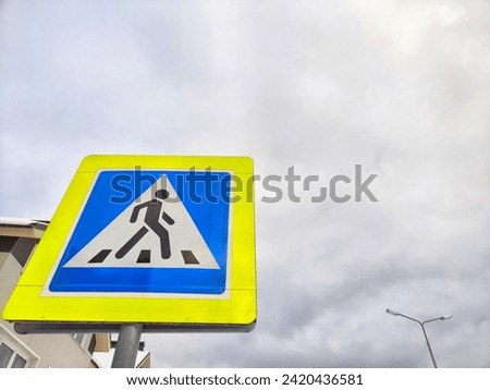 A pedestrian crossing sign on the background of a gray sky with clouds. Drawing, pictogram for pedestrians crossing the road