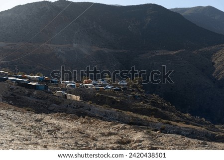 Post-2023 earthquake, a rural village on the Atlas Mountains' slopes near Amizmiz, Morocco. Inhabitants face harsh conditions, living in colorful tents among rocks under power lines.  Royalty-Free Stock Photo #2420438501