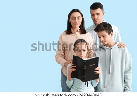 Family with Holy Bible praying together on blue background Royalty-Free Stock Photo #2420443843