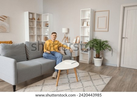 Young man sitting on grey sofa in living room