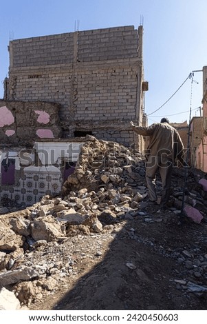 Devastation aftermath: a person inspects a severely damaged building. Debris and rubble surround, revealing extensive structural damage in a sunlit urban area.