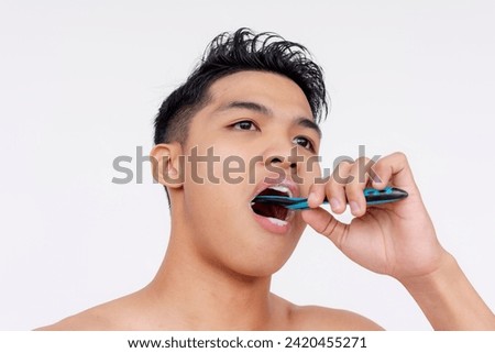 Close-up of a young man without a shirt brushing his lower molars and teeth, focused on oral hygiene and dental care. Royalty-Free Stock Photo #2420455271