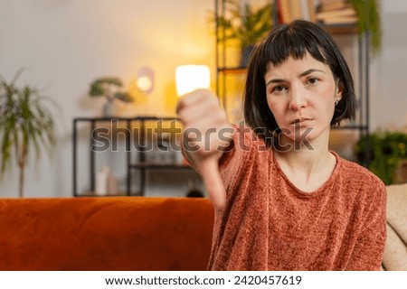 Portrait of upset Caucasian woman showing double thumbs down sign gesture, expressing discontent disapproval dissatisfied bad work dislike sitting in living room at home. Girl sits on sofa. Copy-space Royalty-Free Stock Photo #2420457619