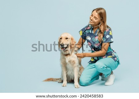 Full body young smiling happy veterinarian woman she wearing uniform heal exam retriever dog using stethoscope isolated on plain pastel light blue background studio portrait. Pet health care concept