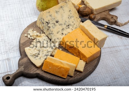 English cheeses collection, mature and coloured cheddar cheese and semi-soft, crumbly old stilton blue cheese close up on plate Royalty-Free Stock Photo #2420470195