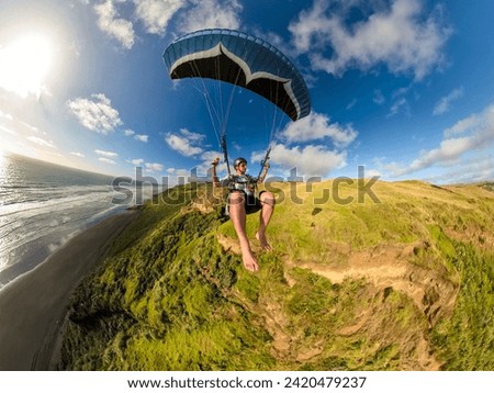 Extreme paragliding pilot soaring in the New Zealand beach at sunset. Adventure concept Royalty-Free Stock Photo #2420479237