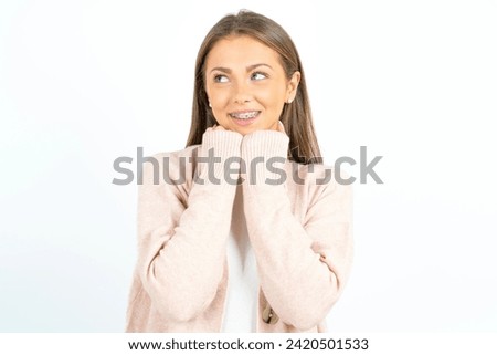 Young beautiful woman standing over white studio background holds hands under chin, glad to hear heartwarming words from stranger