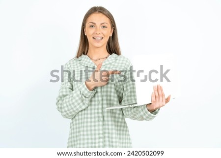 Shocked Young beautiful woman wearing green plaid pyjama pointing finger modern device. Listening to a streaming podcast. 