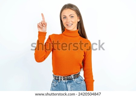 Young beautiful woman standing over white studio background pointing finger up and looking inspired by genius thought, showing good idea sign, having clever solution in mind