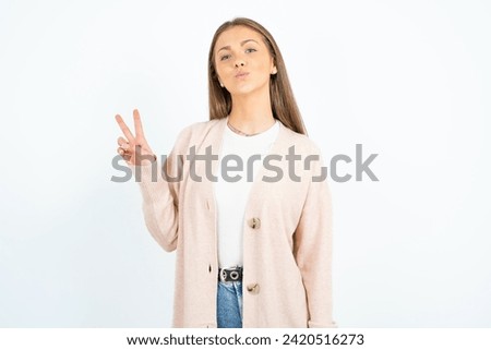 Young beautiful woman  makes peace gesture keeps lips folded shows v sign. Body language concept