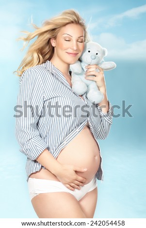 Beautiful pregnant woman with teddy bear in the clouds. Design of toy is altered.