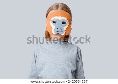 A boy playing in a monkey mask on a gray background. Child mask fun for Halloween holiday or carnival. High quality photo