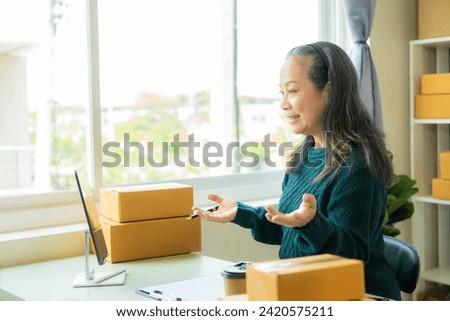 Senior Asian woman doing online shopping at home with boxes and laptop to take orders, name and deliver packages
