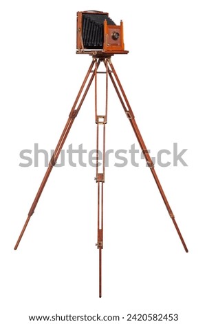 An antique wood camera with bellows atop an old wooden tripod isolated on white