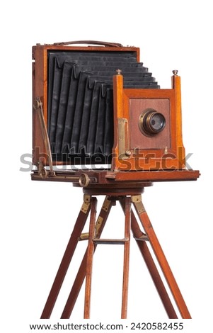 An antique bellows camera atop an old wooden tripod isolated on white