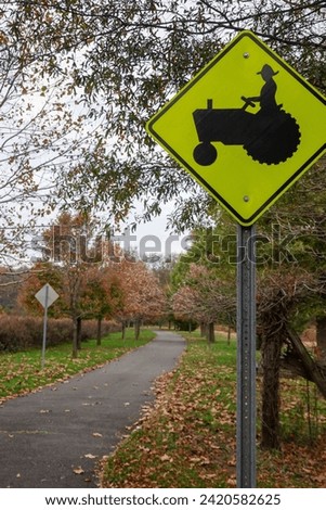 Fluorescent green triangular yield sign with the silhouette of a farmer on a tractor near a country walking path near trees