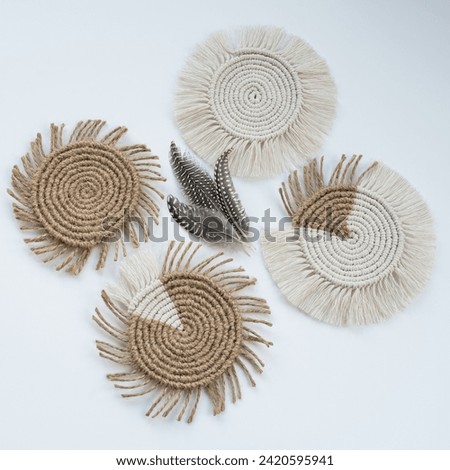 Four diamond-shaped macramé coasters with a central arrangement of three gray and white quail feathers. A unique and elegant composition against a white backdrop. Royalty-Free Stock Photo #2420595941