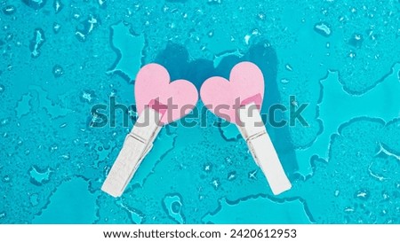 two little pink hearts in clothespins on blue background with drops of water. Creative San Valentine composition Royalty-Free Stock Photo #2420612953
