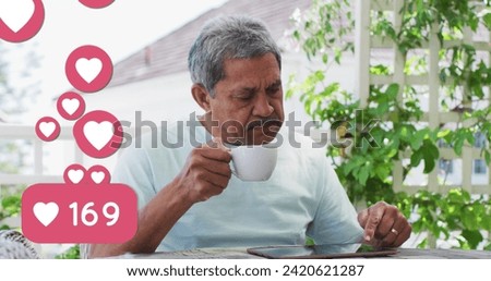 Image of heart love icons over senior man using tablet, drinking coffee at home. global social media networking, connection and communication concept digitally generated image.