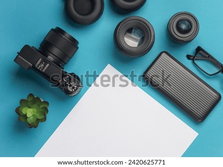 Camera and accessories with white blank sheet of paper for text on blue background