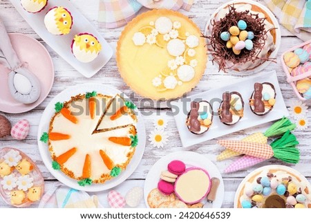 Easter or spring dessert food table scene. Top down view over a white wood background. Lemon tart, cupcakes, Easter egg and carrot cakes and a variety of sweets. Royalty-Free Stock Photo #2420646539