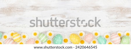 Easter eggs and white daisy flowers. Top view bottom border against a rustic white wood banner background. Copy space.