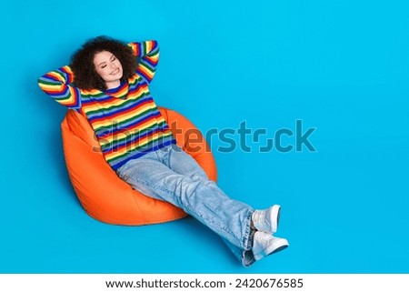 Full size photo of pretty young girl sit beanbag hands behind head dressed stylish rainbow print outfit isolated on blue color background