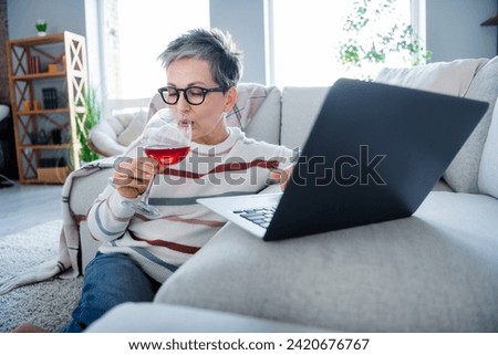 Photo of lovely aged person sit carpet floor drink wine use netbook spend free time apartment indoors
