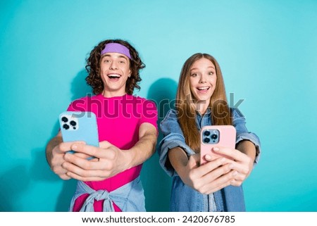 Photo of two funny happy brother and sister takes selfie pictures themselves holding phones smiling isolated on cyan color background