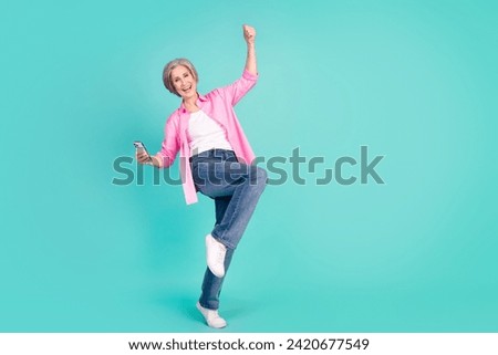 Full size photo of satisfied pensioner person stand one leg holding smartphone win lottery yell isolated on turquoise color background