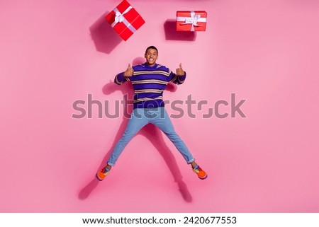 Full length photo of handsome young guy jump show thumb up gifts dressed stylish violet striped garment isolated on pink color background